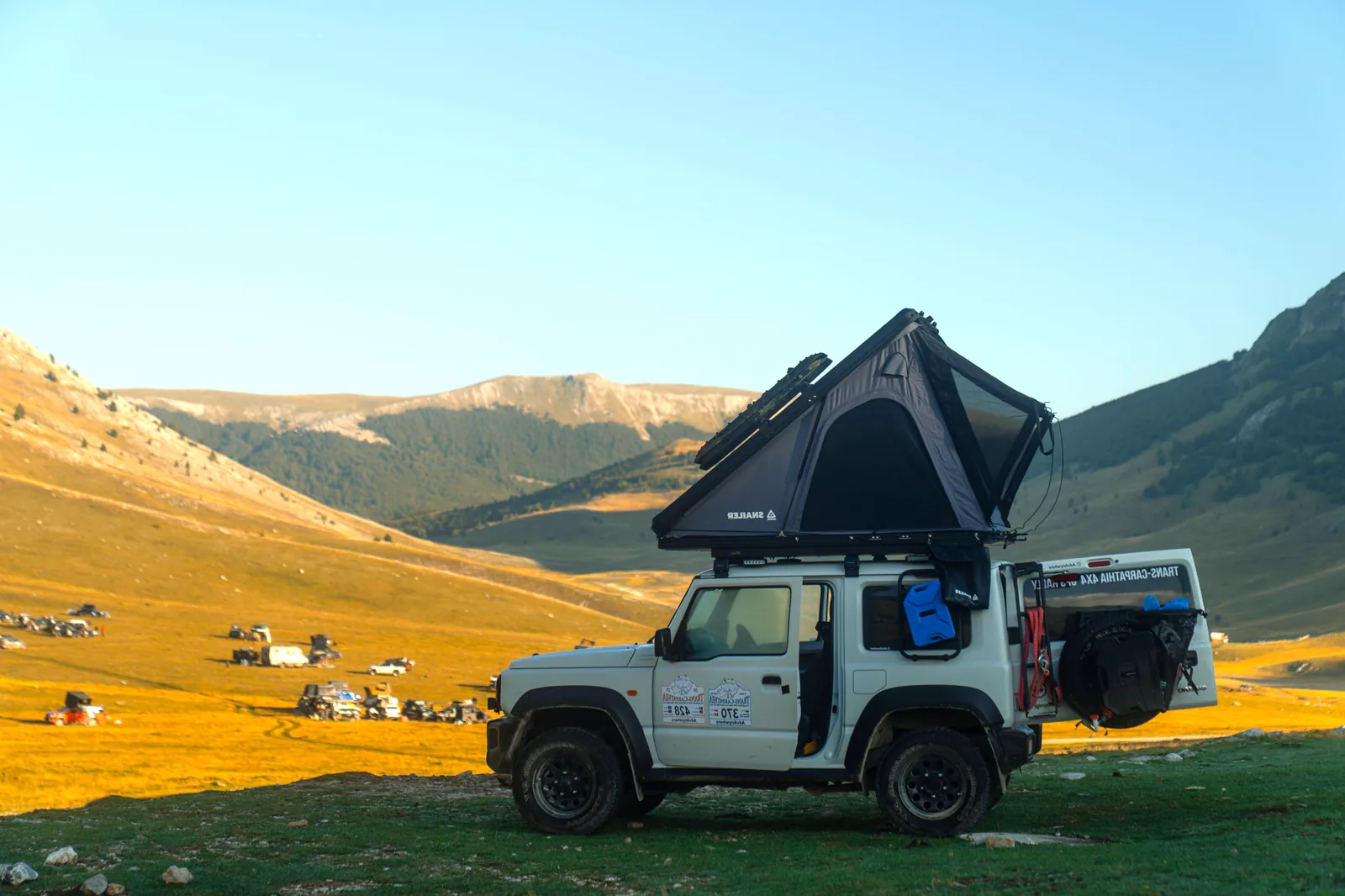 Off-road vehicle with an open SNAILER roof tent at a mountain campsite